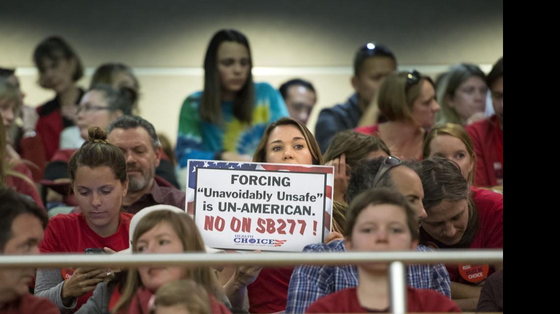 
A woman who was against Senate Bill 277 holds a sign before the first hearing in the Senate Health Committee on April 8. A large group filled the room and many waited outside.
