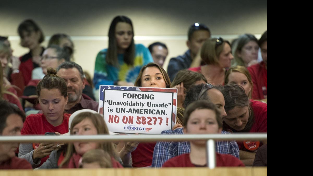 
A woman who was against Senate Bill 277 holds a sign before the first hearing in the Senate Health Committee on April 8. A large group filled the room and many waited outside.
