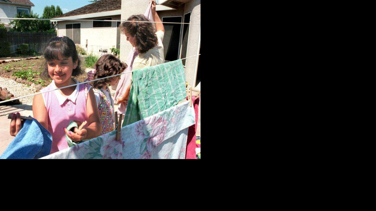 
Two daughters help their mom Jennifer Khal take down the wash from the clothesline in the backyard.
