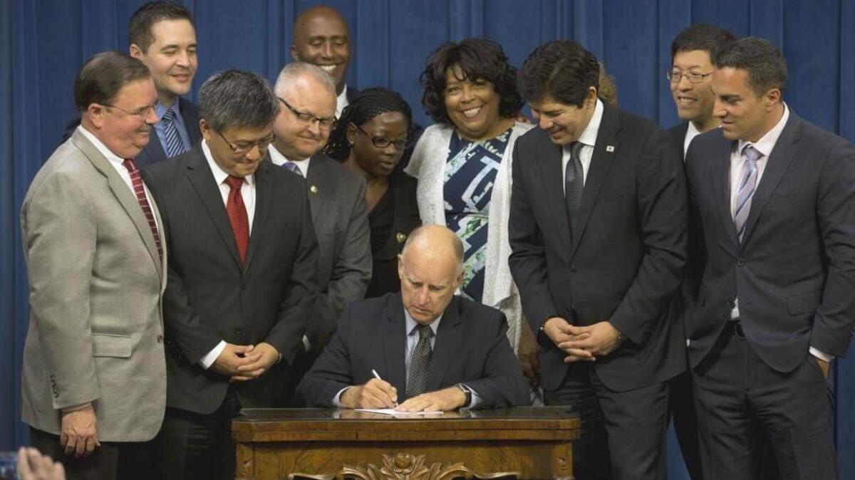 Gov. Jerry Brown signs legislation that will automatically enroll millions of private-sector workers in retirement saving accounts, as lawmakers and supporters look on, at the Capitol Thursday, Sept. 29, 2016, in Sacramento, Calif.