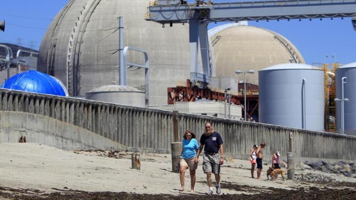 In this June 30, 2011, file photo, beach-goers walk on the sand near the San Onofre nuclear power plant in San Clemente, Calif. The plant was shut down in 2012.
