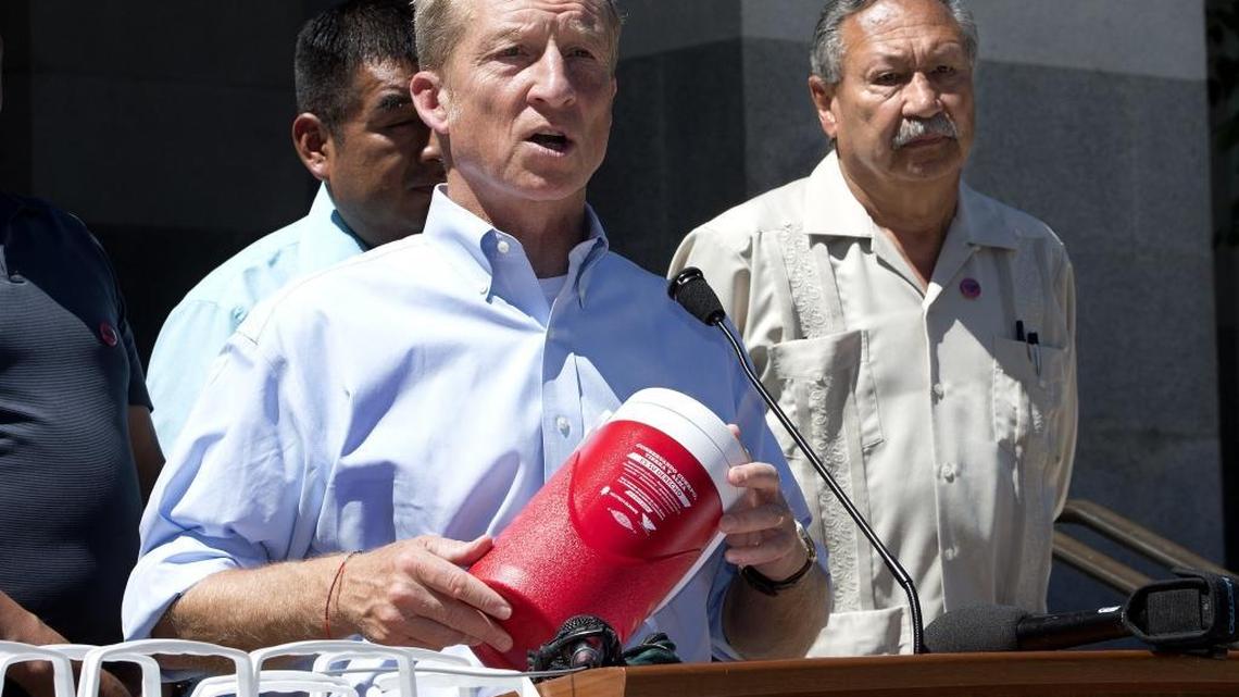 Tom Steyer, center, holds one of more than 1,000 water bottles being given to farm workers to help deal with the summertime heat, June 29, 2016, in Sacramento.