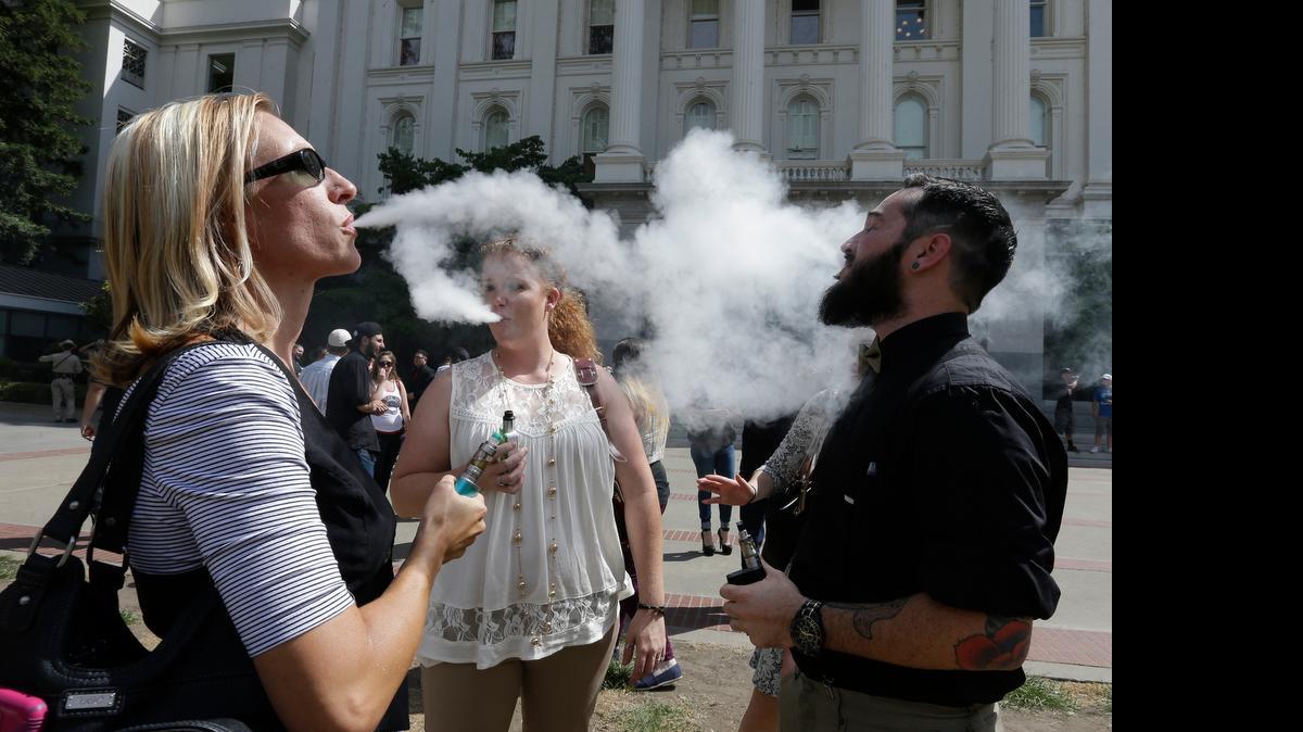 
Kari Hess, left, co-owner of Nor Cal Vape in Redding, vapes with Jackie Voisione, center, and Michael Ventura, an e-liquid manufacturer from San Diego, at the Capitol.


