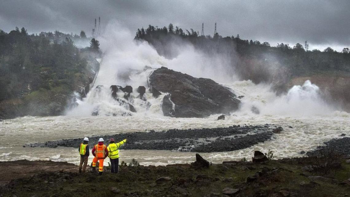 A Cal Fire firefighter, right, talks to workers on the Oroville Dam project in front of the dam spillway, fractured because of high water releases, on Feb. 20, 2017.