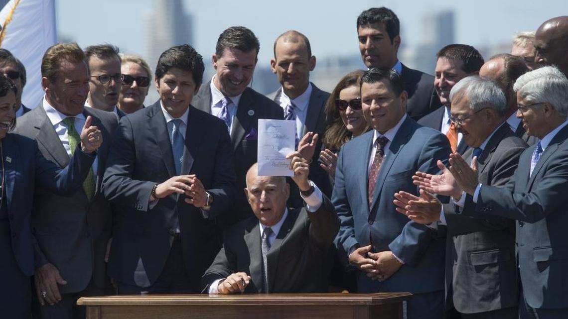 Gov. Jerry Brown raises the signed bill extending the cap-and-trade climate change program until 2030 on July 25, 2017 on Treasure Island.