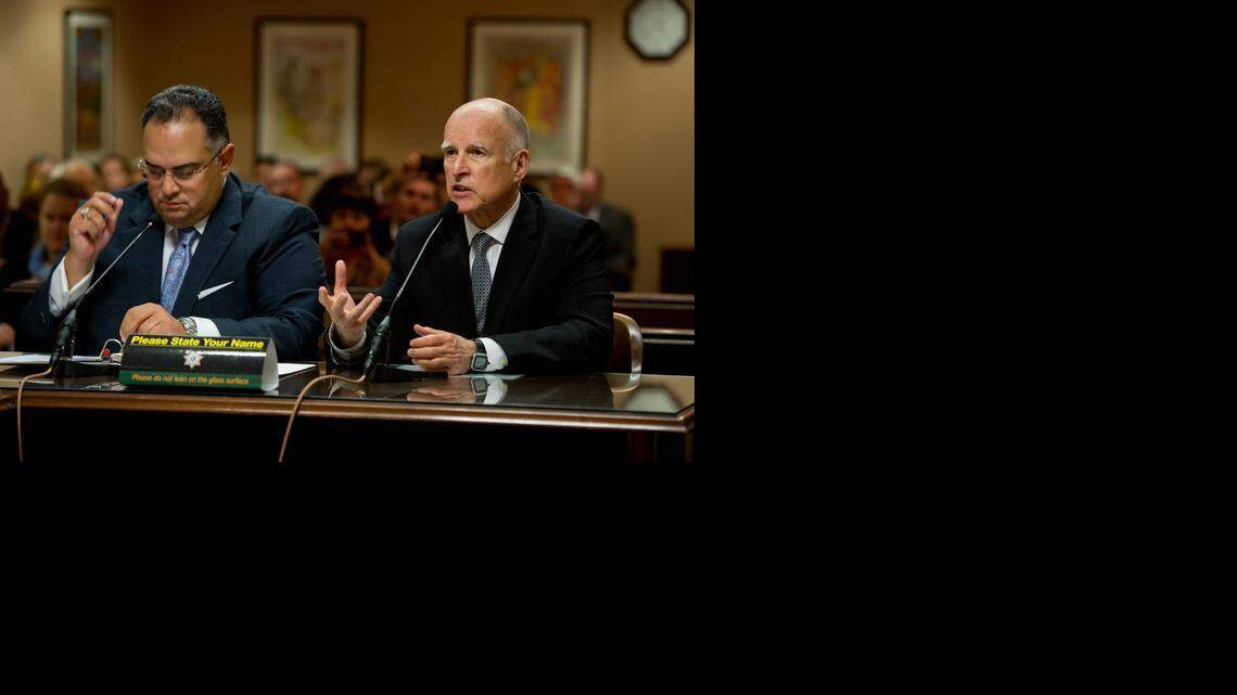 California Gov. Jerry Brown and then-Speaker of the Assembly John Pérez speak to an Assembly committee to promote the plan to create a rainy-day fund. Voters later approved a ballot measure, yet now the administrative interpretation of the law could change the amount set aside by billions of dollars.