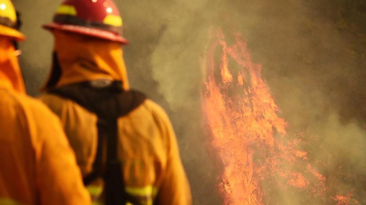 In this photo provided by the Santa Barbara County Fire Department, firefighters keep an eye on flames as pockets of unburned vegetation flare up off Bella Vista Dr. in Montecito, Calif., Wednesday, Dec. 13, 2017.
