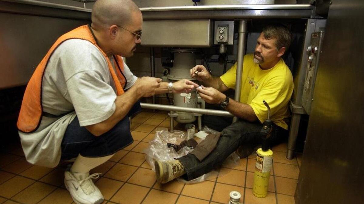 California State Prison Sacramento plumber Richard Williams (right) works with inmate Mario Herrera installing a new kitchen faucet at the facility.