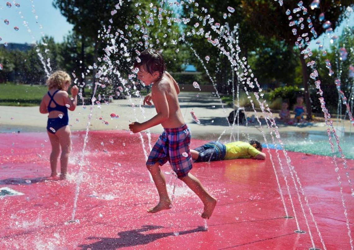 Josh Newton, 5, center, and his sister, Cecilia Newton, 3, left, of Rancho Cordova cool off in a water feature at Village Green Park during a June heat wave.