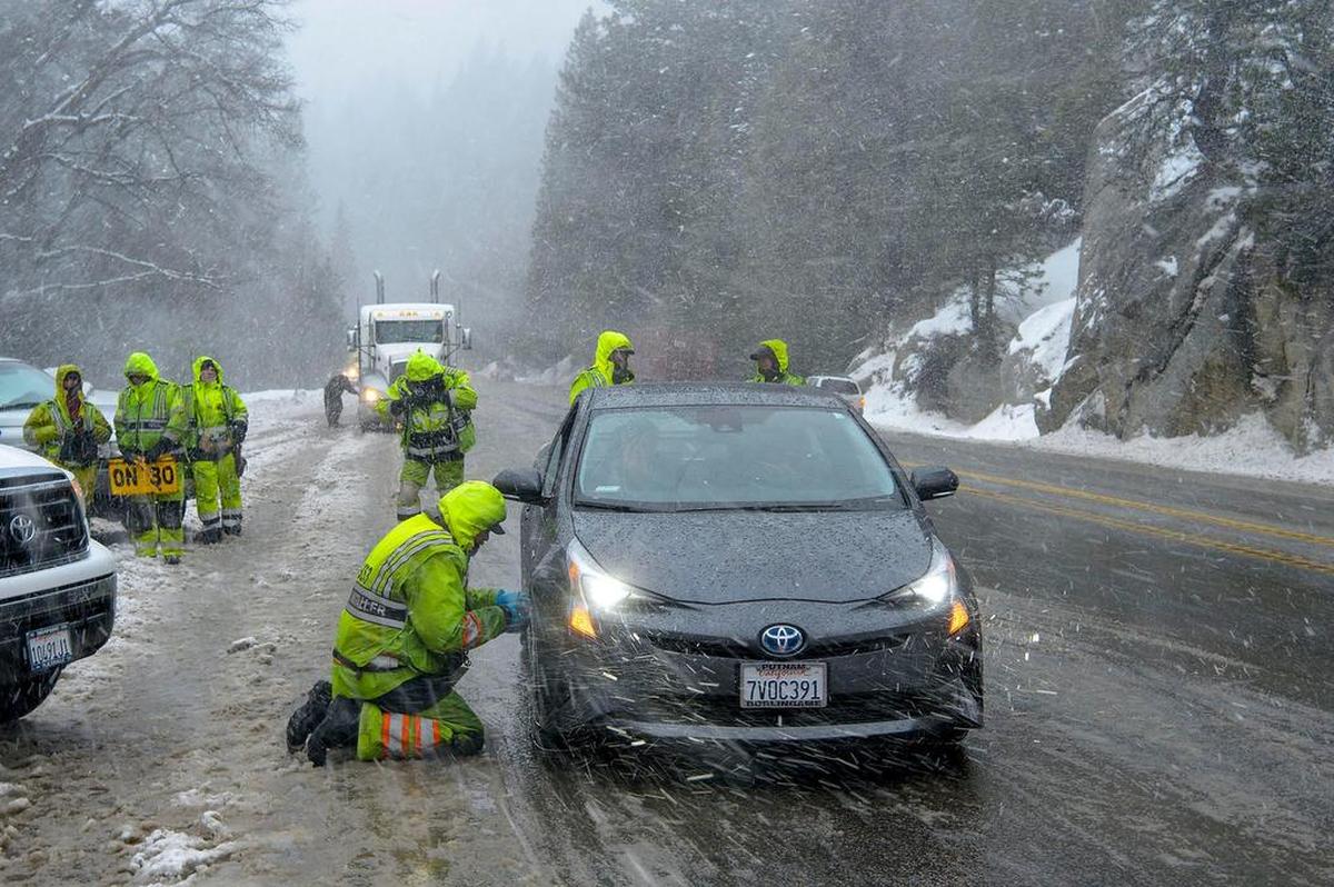 Chain installers work under heavy snow conditions along Highway 50 near Kyburz in El Dorado County. Whiteouts made Sierra travel perilous.