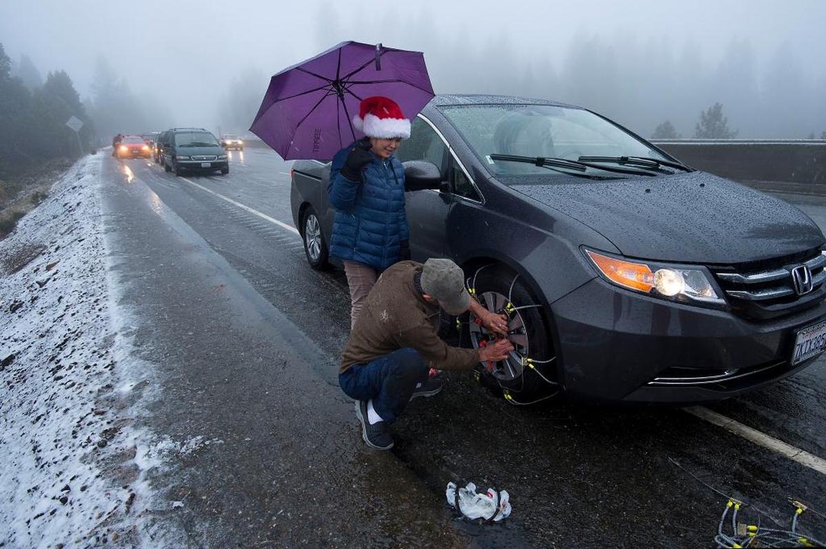 As the snow falls, Holly Ly, left, and Charles Luong of San Diego, struggle to put tire chains on their car in Camino on Thursday, Dec. 24, 2015.