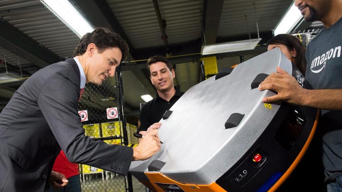 Canada's Prime Minister Justin Trudeau signs a robot used by Amazon at the company's new fulfillment center, in Brampton, Ontario, Canada, Oct. 20, 2016. (Nathan Denette/The Canadian Press via AP)