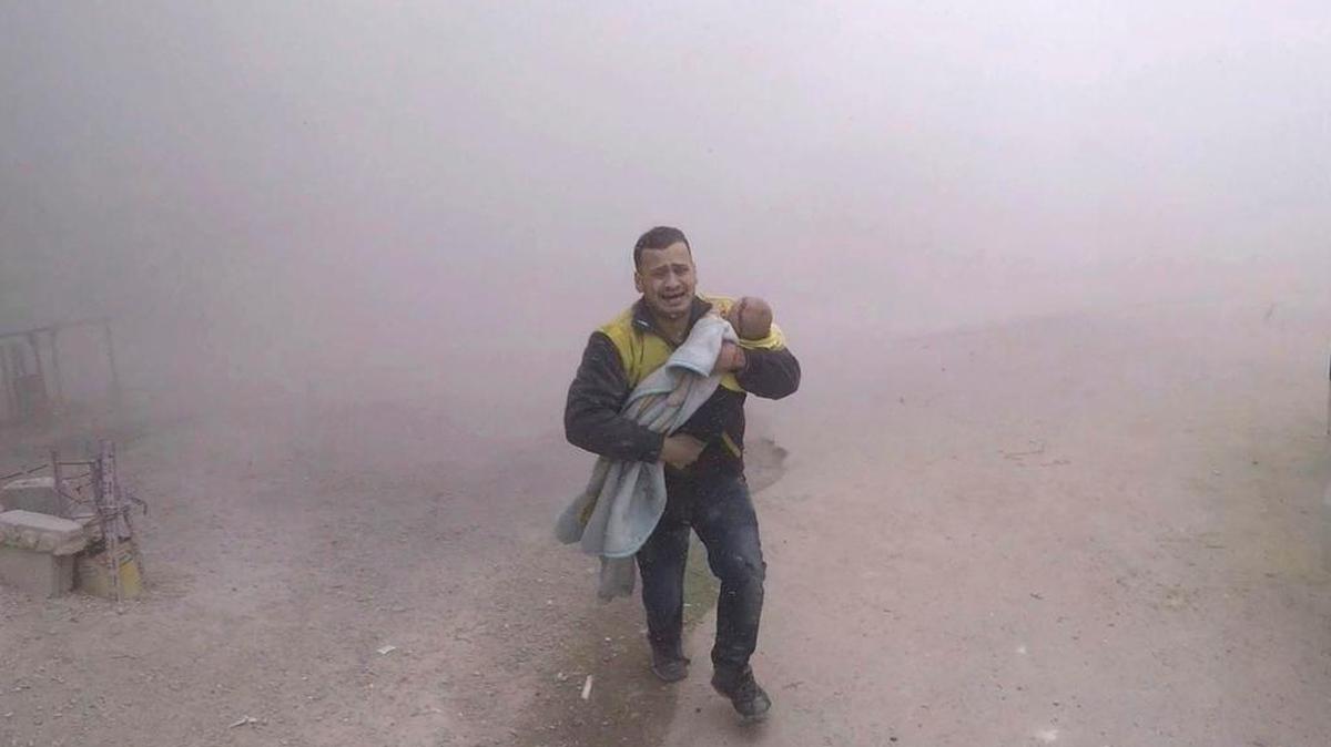 A paramedic for the Syrian Civil Defense group known as the White Helmets, carries his wounded son as airstrikes hit a rebel-held suburb near Damascus, Syria, Tuesday, Feb. 6, 2018, according to the organization, which provided this picture. Bombings and civilian atrocities have been ongoing, notwithstanding the recent suspected sarin gas attacks, which on Friday prompted President Donald Trump to order retaliatory airstrikes. (Syrian Civil Defense White Helmets via AP)