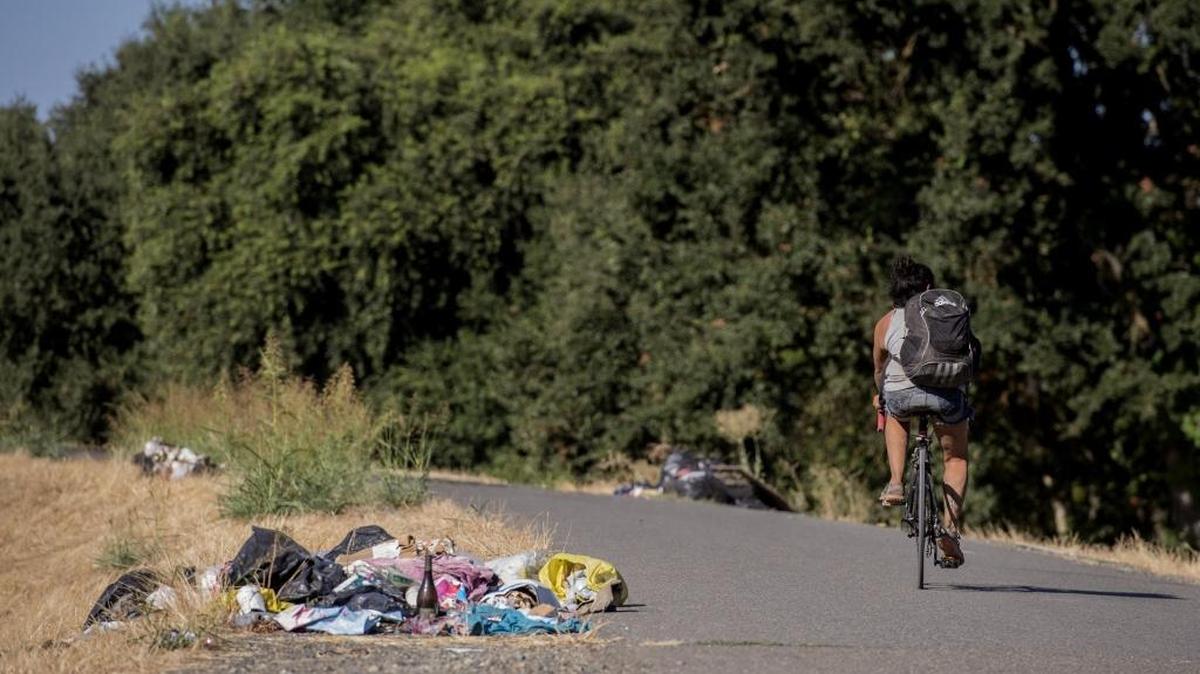 A bicycle rider rides past piles of trash left by the homeless camps near the end of Jefferson Ave and the American River on Friday, August 25, 2017