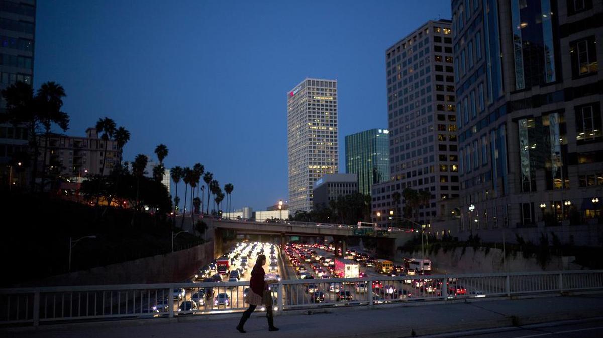 A woman walks on a bridge as heavy traffic moves along the 110 Freeway during rush hour in Los Angeles.