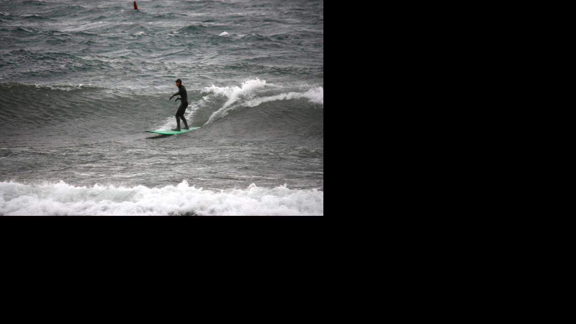 
A lone surfer catches a wave caused by high winds in Lake Tahoe on Thursday. Winds gusted to 140 mph through the Sierra ahead of a powerful Pacific storm, damaging homes and a church in South Lake Tahoe, closing schools, and grounding commercial airline flights in Reno.
