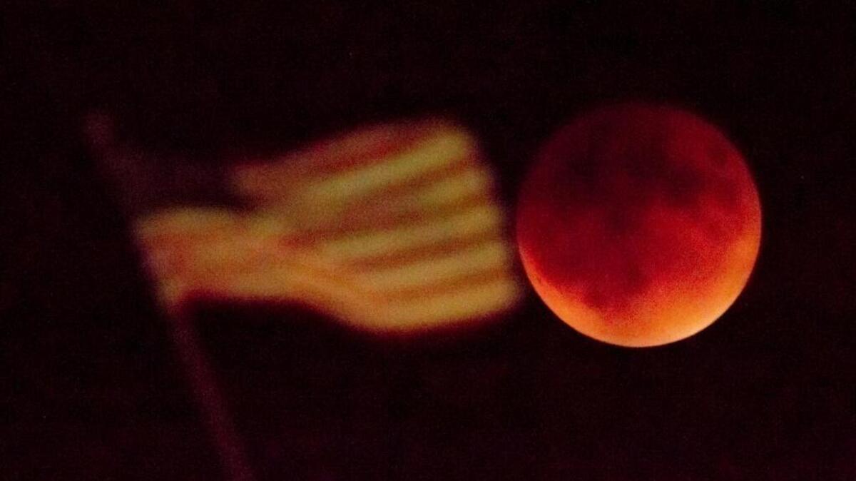 
A totally eclipsed supermoon rises beyond a U.S. flag Sunday in Kansas City, Mo. It was the first time that the events have made a twin appearance since 1982, and they won’t again until 2033.
