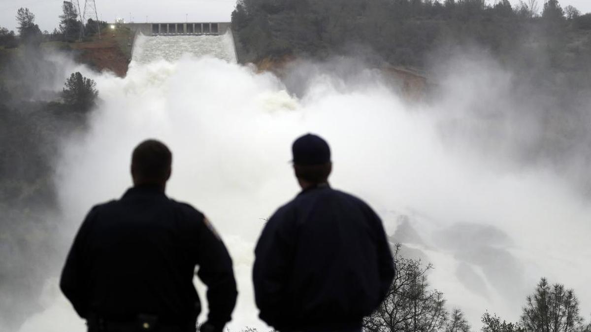 Two men watch as water gushes from the Oroville Dam's main spillway Wednesday. The Oroville Reservoir is continuing to drain as state water officials scrambled to reduce the lake's level ahead of impending storms.