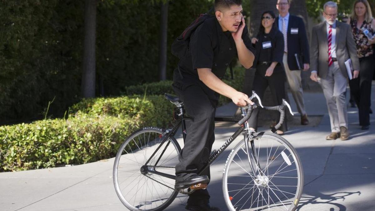 A man talks on his cellphone while riding his bicycle past pedestrians along businesses in midtown Sacramento.