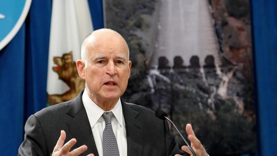 California Gov. Jerry Brown discusses his proposal to spend $437 million on flood control and emergency response in the wake of recent storms, during a news conference Friday in Sacramento. In the background is a photograph showing the hole in the main spillway of Oroville Dam.
