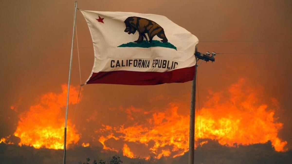 The state flag flies next to a home on Highway 94 south of Potrero in San Diego County on Monday, June 20, 2016, as huge flames roar behind it. An intensifying heat wave stretching from the West Coast to New Mexico threatened to make the fight against Southern California wildfires more difficult.