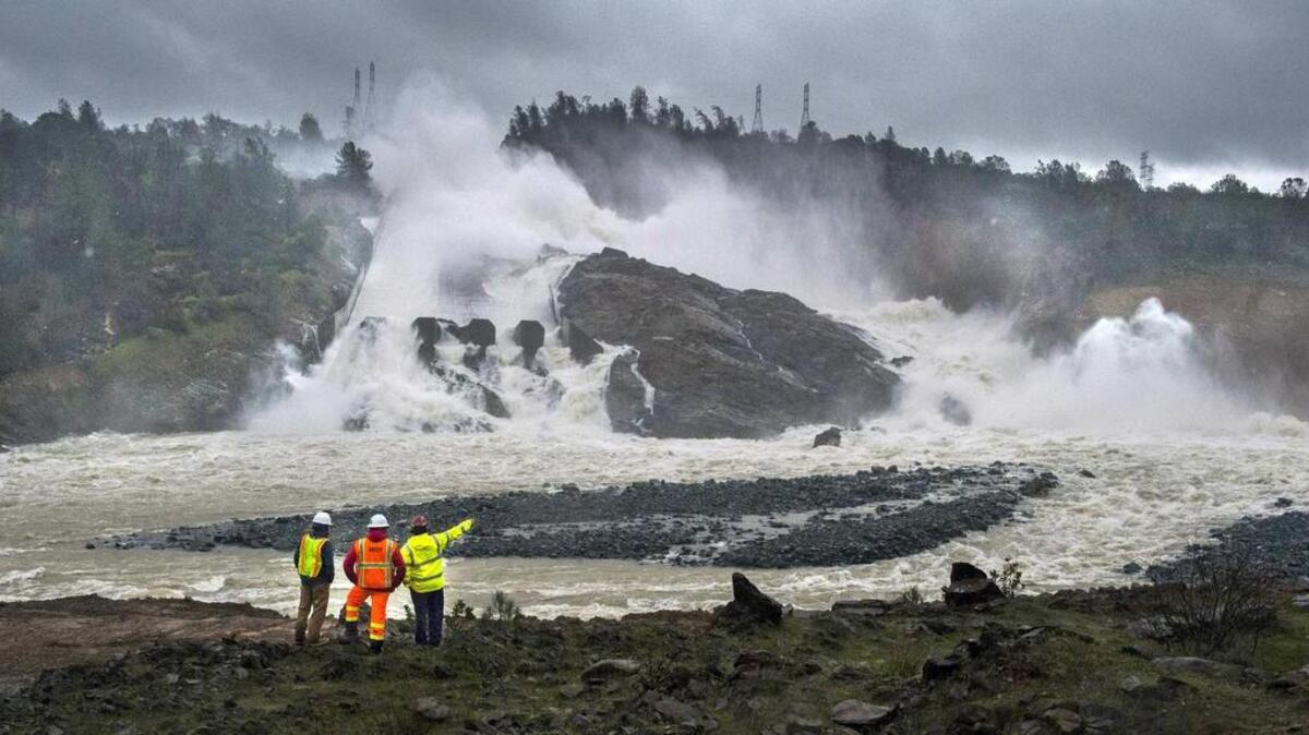 Workers and a firefighter watch water pouring down Oroville Dam’s damaged main spillway on Feb. 20.