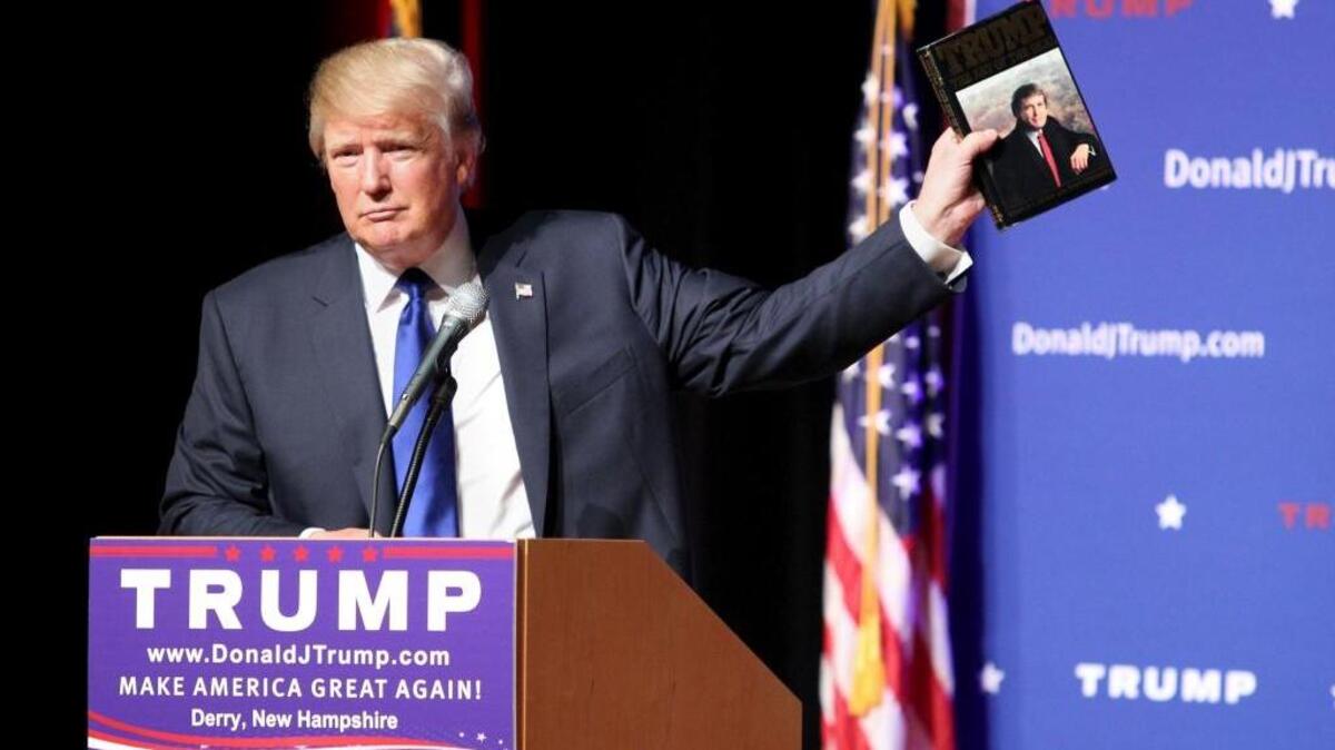 Republican presidential candidate Donald Trump holds up a copy of his 1987 book, “Trump: The Art of the Deal,” during a town hall event.