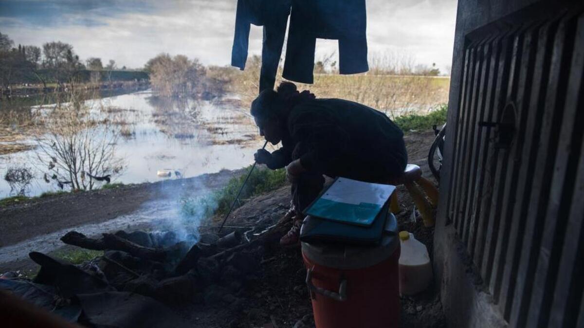 A homeless woman who did not want to be identified blows air on a fire after she washed some pants to help dry them at an encampment under the Norwood Avenue bridge in North Sacramento.