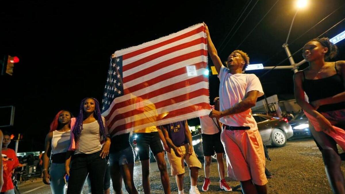 Protesters carry an American flag chanting “all lives matter” as they congregate at the Triple S convenience store in Baton Rouge, La., on Wednesday after Alton Sterling, 37, was shot and killed outside the store by Baton Rouge police, where he was selling CDs.