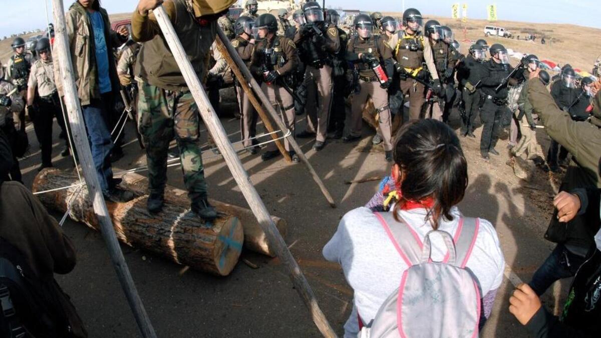 Protesters shield their faces as a line of law enforcement officers holding large canisters with pepper spray shout orders to move back during a standoff in Morton County, N.D., last week.