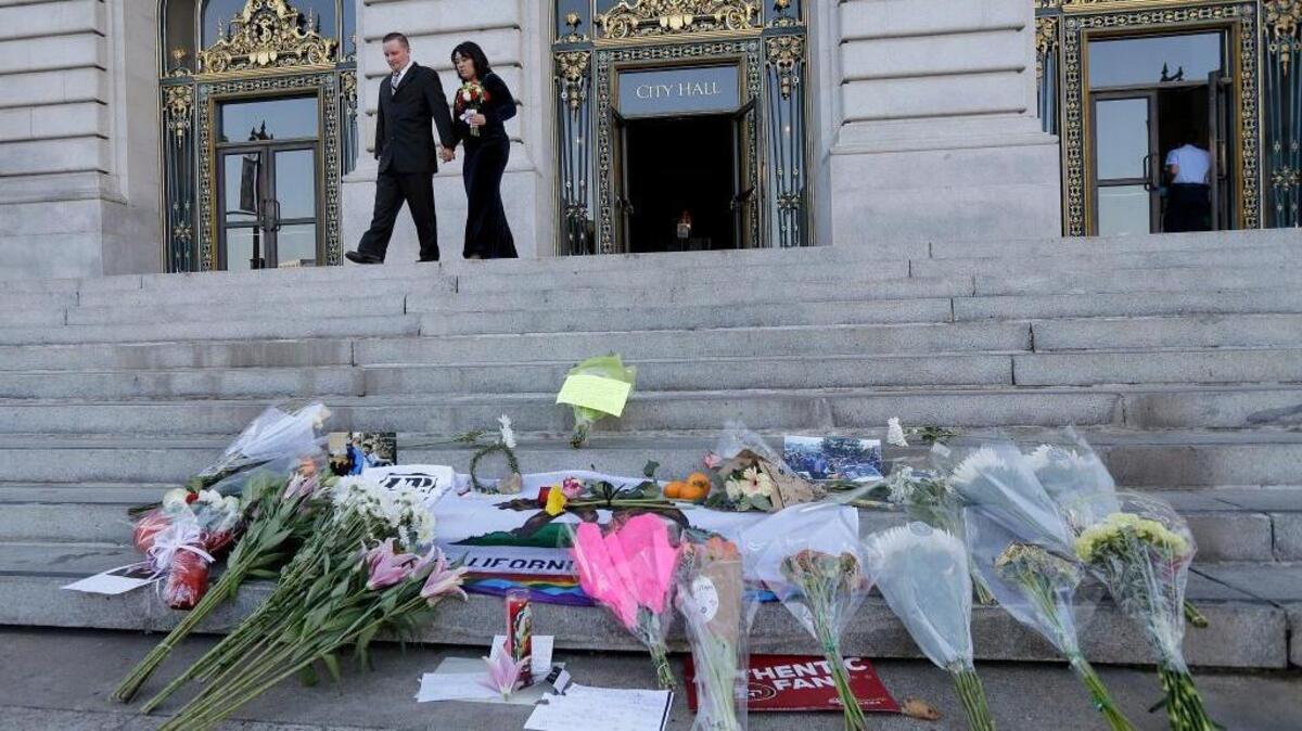 Newlyweds Gary Thomas and Mary Wong-Thomas walk behind flowers and signs left for Mayor Ed Lee on the steps of City Hall in San Francisco. Lee, who led a technology-driven economic boom in San Francisco, died unexpectedly early Tuesday at age 65.