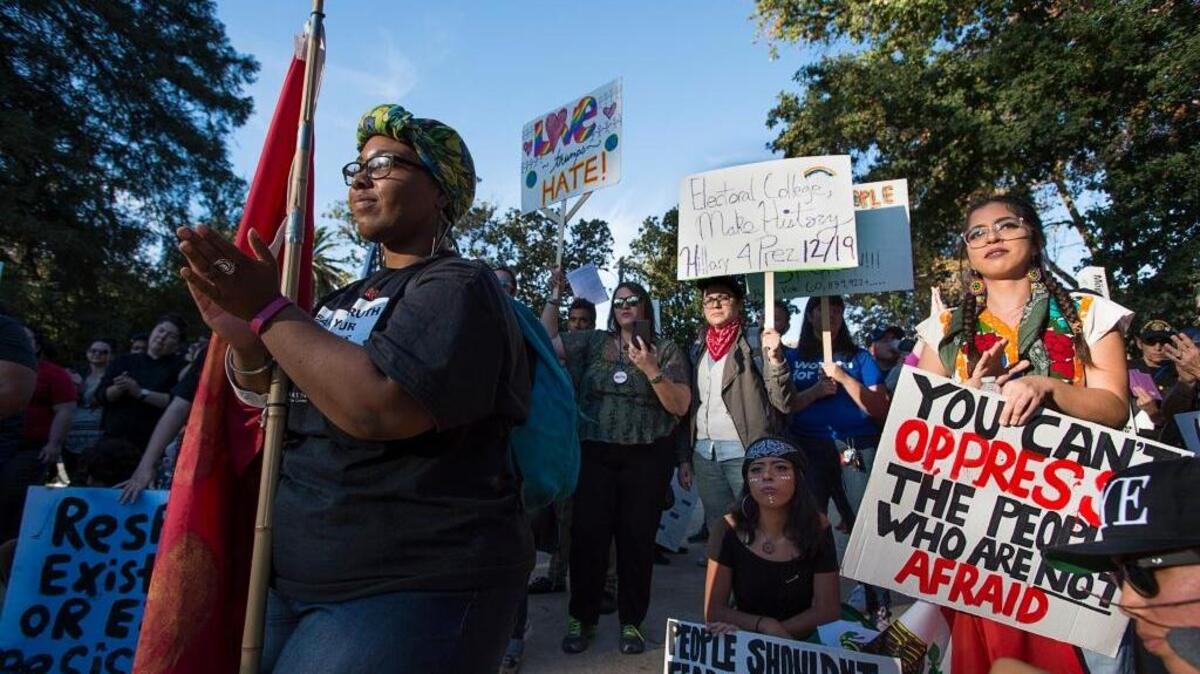 Myree Hall, a member of the ANSWER Coalition Party for Socialism and Liberation, applauds Sunday after listening to a speaker with a coalition of protesters against President-elect Donald Trump at Sutter’s Fort in Sacramento.