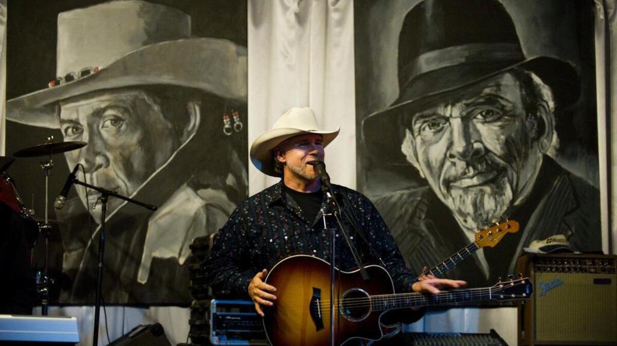 Tom Rockwell plays in 2012 at an Oildale club in front of paintings of the Bakersfield country music greats, Buck Owens, left, and Merle Haggard.