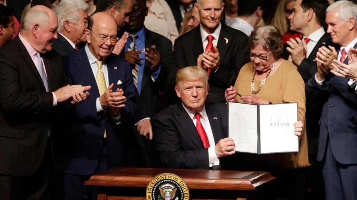 President Donald Trump shows his executive order for a revised policy on trade and tourism with Cuba, surrounded by cabinet members and supporters in Miami on Friday.