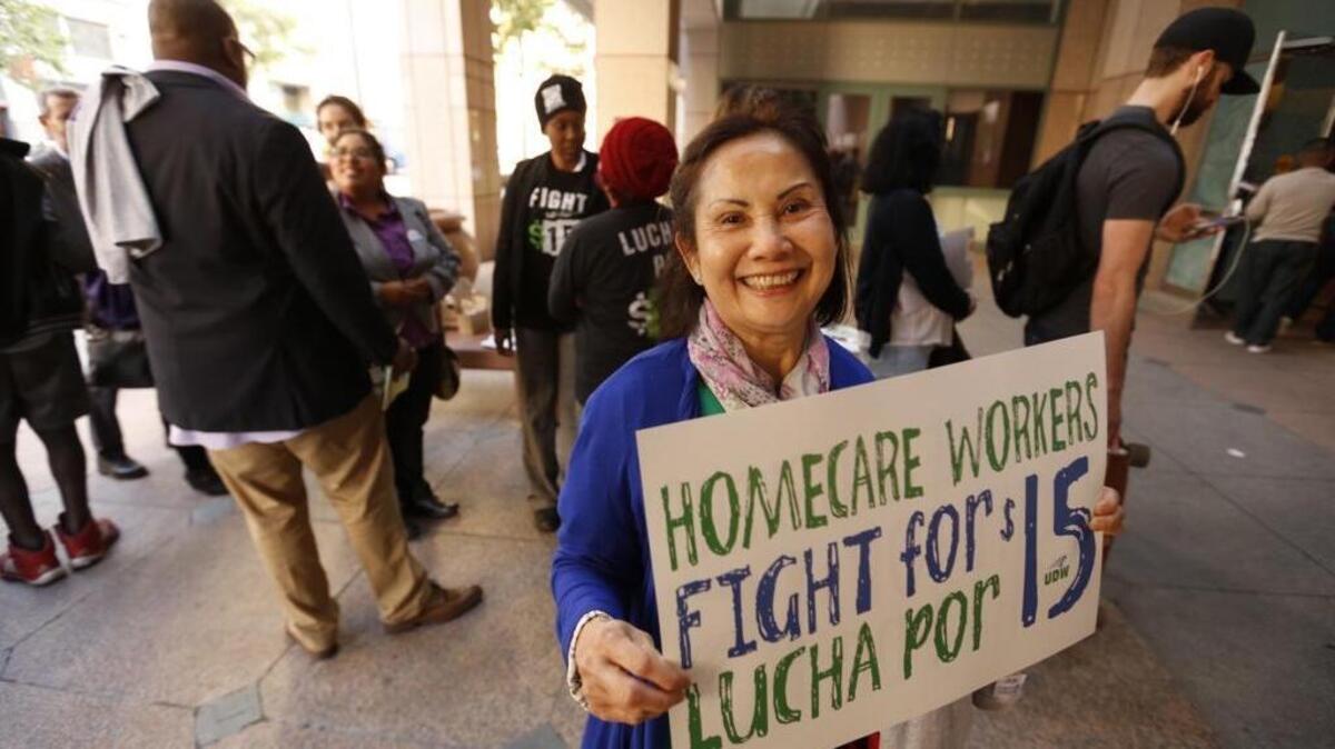 Health care worker Mimi Bui holds a sign as people wait to enter the Ronald Reagan State Building in Los Angeles where Gov. Jerry Brown signed a minimum wage increase on April 4.