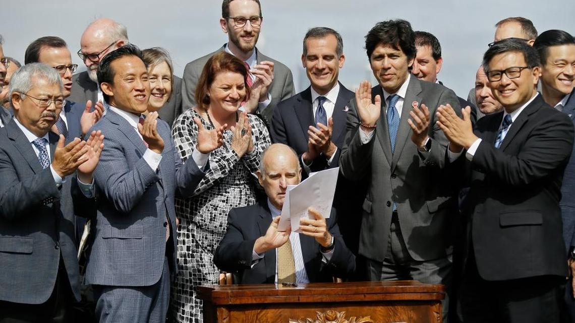 California Gov. Jerry Brown holds up a number of bills he signed to help address housing needs as a group of elected officials and housing advocates applaud Friday in San Francisco. With one of the nation's most expensive cities as his backdrop, Gov. Brown signed legislation Friday aimed at tackling California's growing affordable housing crisis.