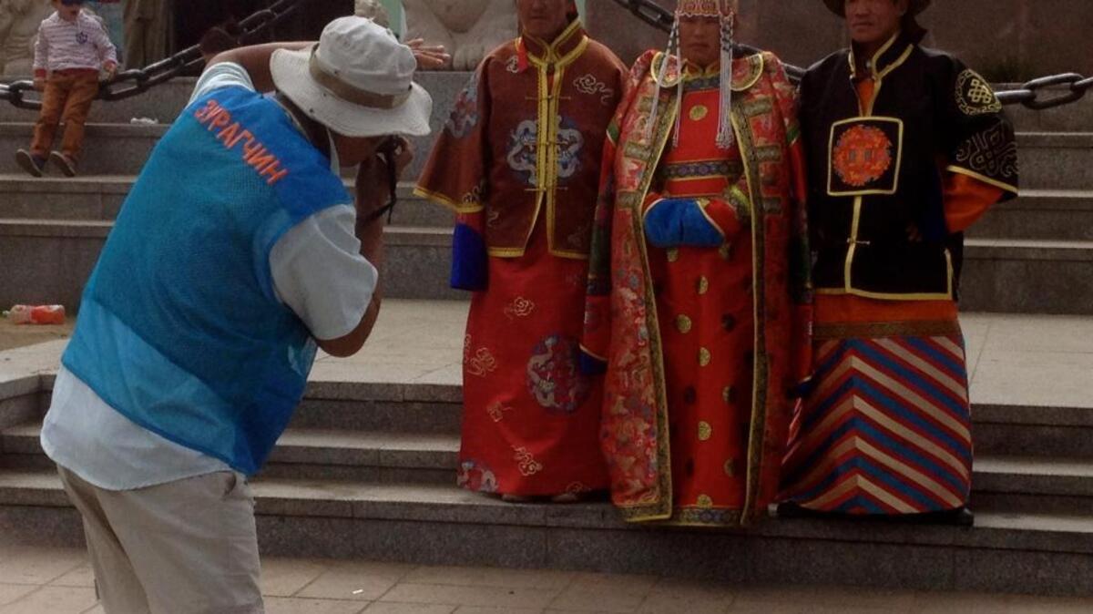 An official photographer, identified as such in Mongolian on the back of his vest, poses customers in period costume at Genghis Khan Square, formerly called Sukhbaatar Square, in Ulaanbaatar, Mongolia, in July 2015.