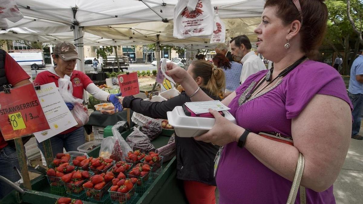 Sandy Nemec of Carmichael, right, buys a bag of cherries with CalFresh coupons at the farmers’ market at Cesar Chavez Park in Sacramento in May 2017.