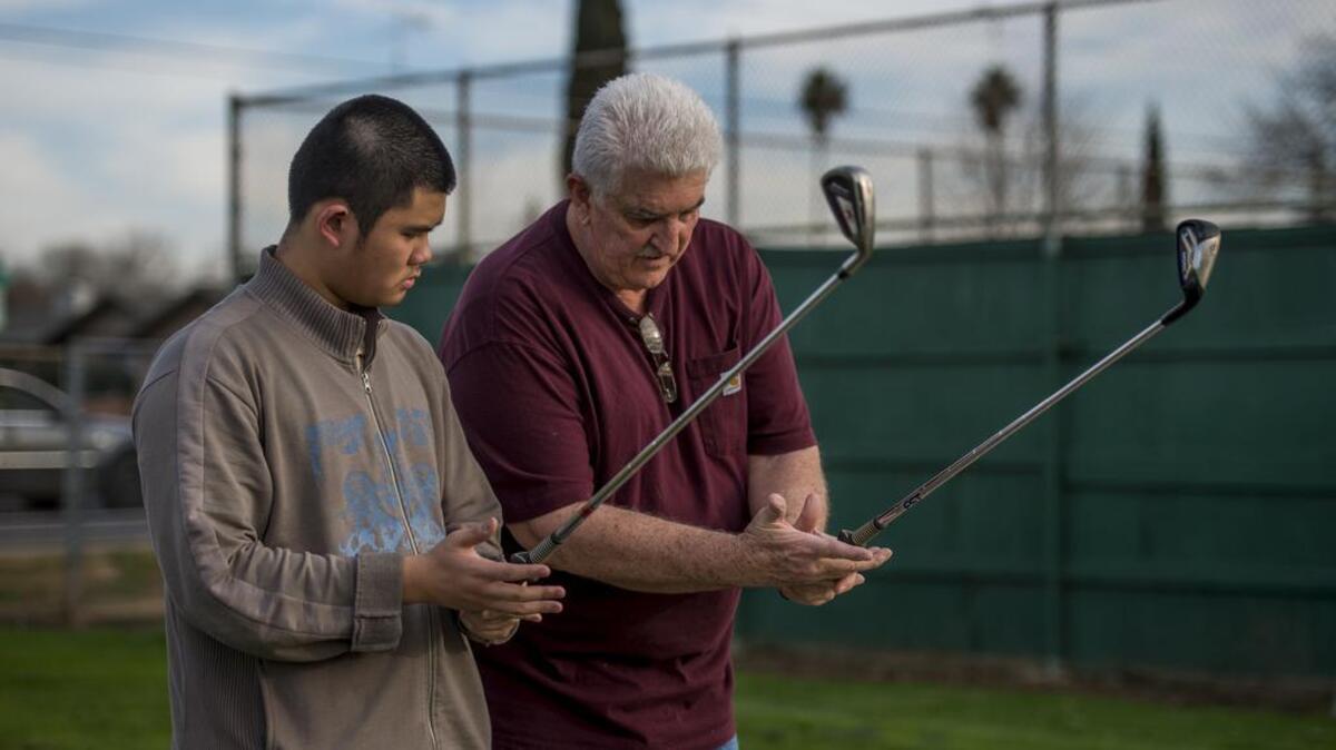 Hiram Johnson assistant golf coach Royden Heitz shows Quan Vuong, who is trying golf for the first time, how to properly grip a gold club.
