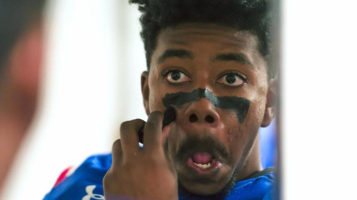Folsom Bulldogs Richard Cornelius (21) puts on face paint as he gets ready inside the locker room.