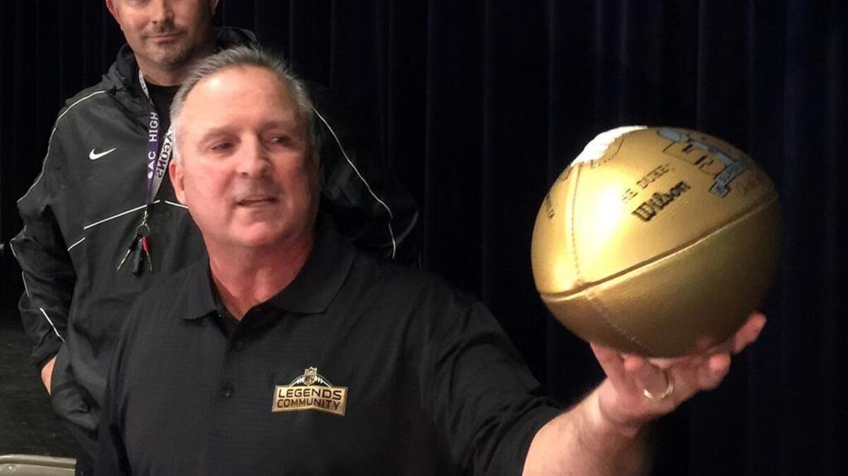 Former Sacramento High School football star Jim Breech displays an NFL-issued ball to commemorate Super Bowl 50. Breech is joined on the Sacramento football team room stage by Dragons coach Justin Reber.
