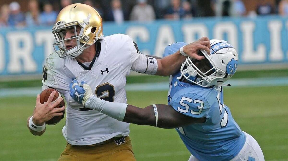 Notre Dame’s Ian Book, left, runs the ball while North Carolina’s Malik Carney reaches for the tackle Saturday in Chapel Hill, N.C. Book, an Oak Ridge High graduate, won in his first start at quarterback for the Irish.