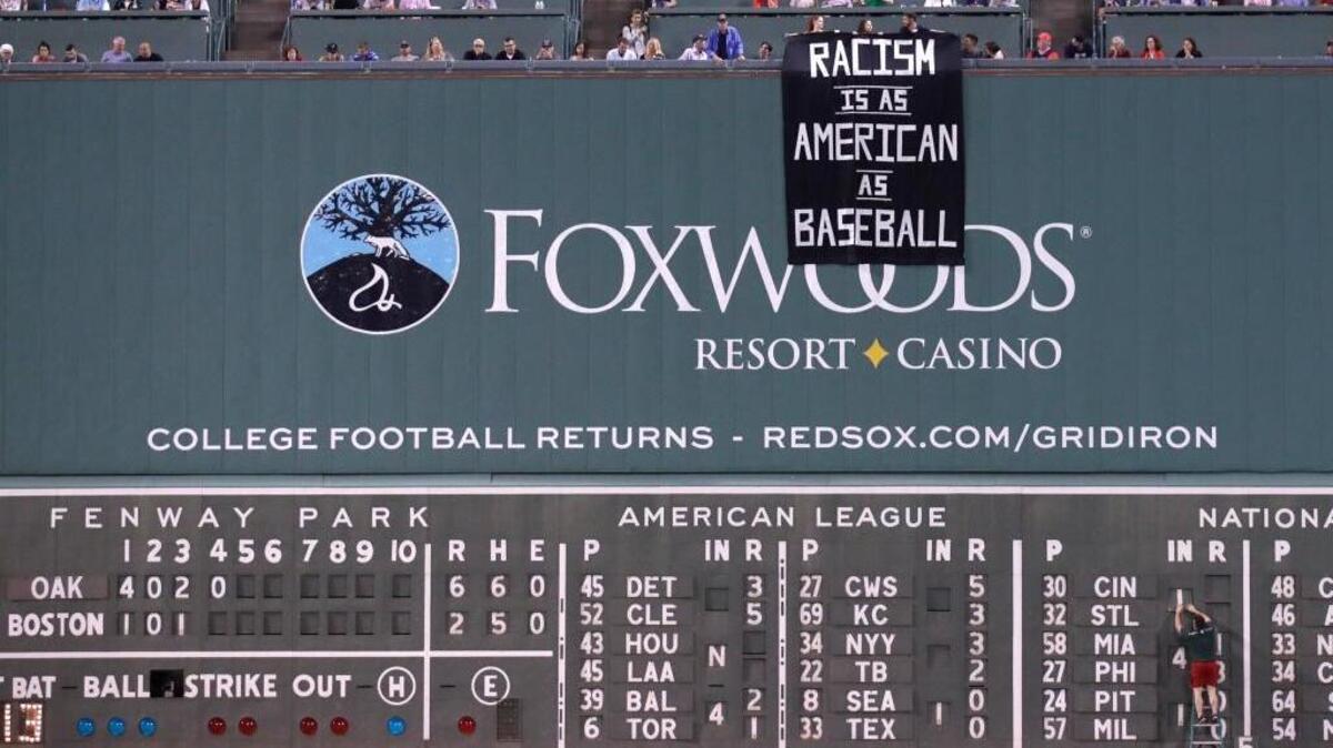 A banner that reads “Racism is as American as baseball” is unfurled over Fenway Park’s Green Monster during the fourth inning of Wednesday’s game between the A’s and Red Sox in Boston.