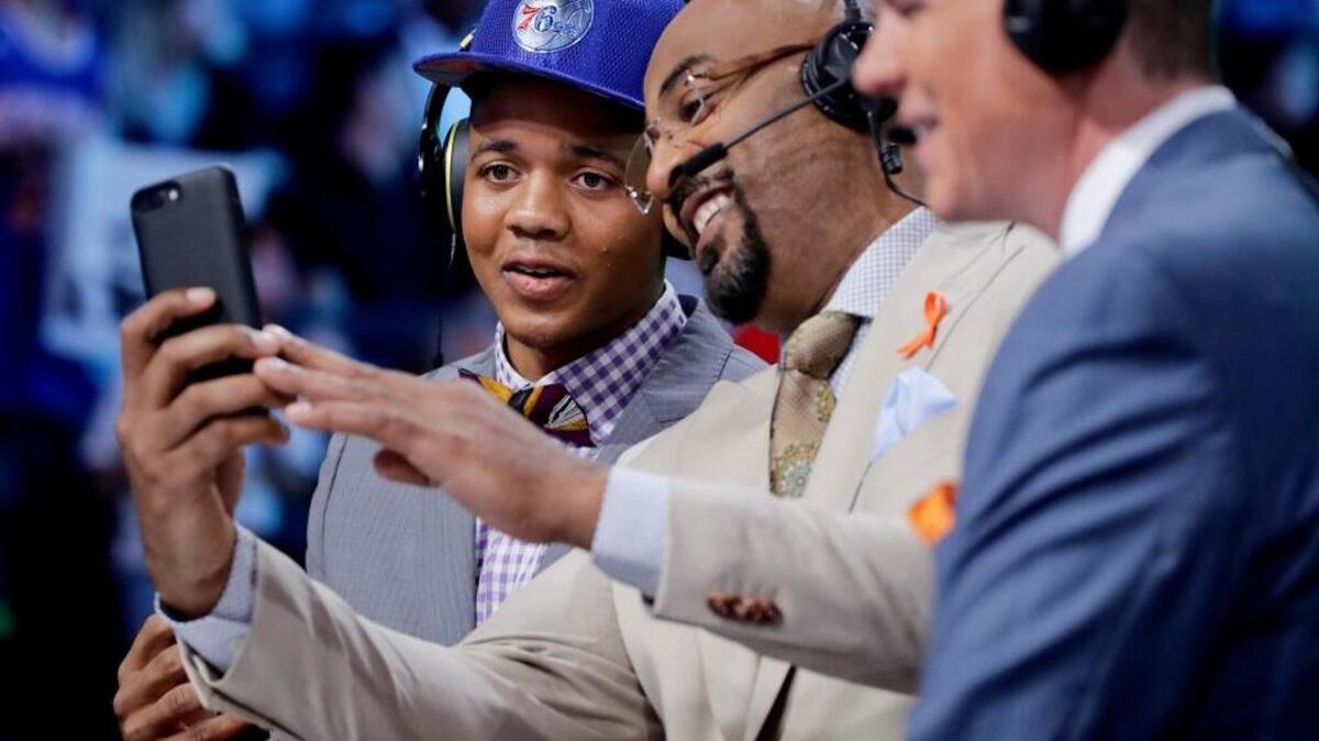 Markelle Fultz, left, looks at a phone with television commentators during the NBA draft Thursday in New York. Could the analysts be pointing out Fultz’s social media error?