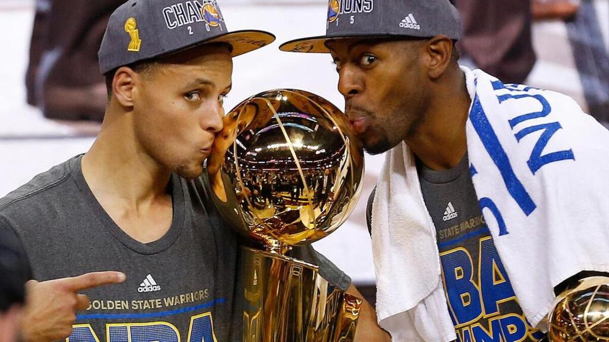 The Warriors’ Stephen Curry, left, and Andre Iguodala kiss the NBA championship trophy last June.