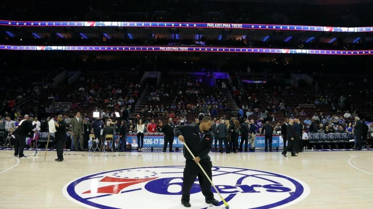 A building worker wipes the court before Wednesday night’s scheduled game between the Kings and Philadelphia 76ers in Philadelphia. The games was postponed because of condensation on the court.