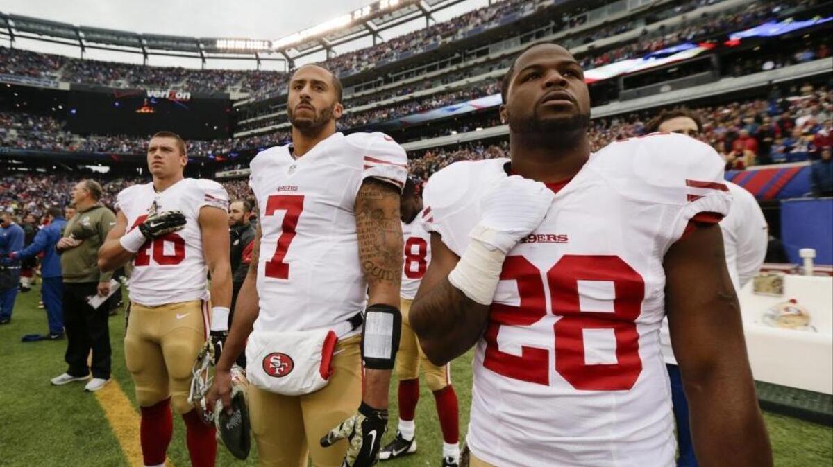 San Francisco 49ers quarterback Colin Kaepernick (7) stands with teammates Derek Carrier (46) and Carlos Hyde (28) during the playing of the national anthem before an NFL football game against the New York Giants Sunday, Nov. 16, 2014, in East Rutherford, N.J.